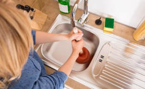 woman trying to unclog sink with plunger 